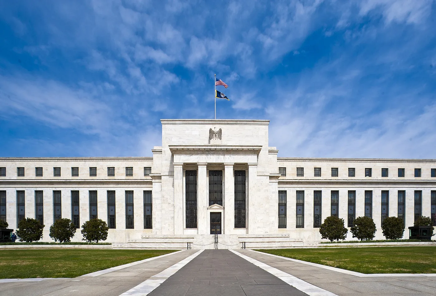 The white marble Marriner S. Eccles Federal Reserve Board Building in Washington, D.C., seen from the street with trees in front.